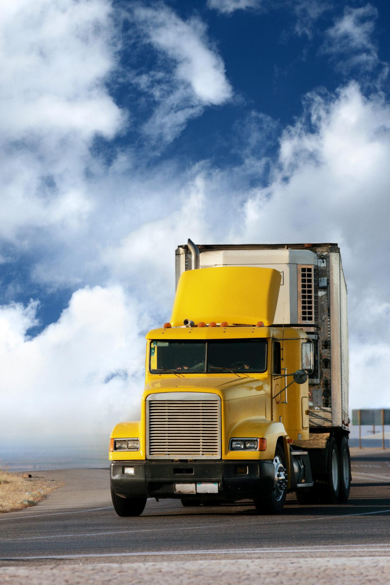 Big yellow trailer on the road over dramatic blue sky with white clouds.